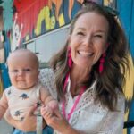 Smiling woman holding a baby in front of a colorful wall