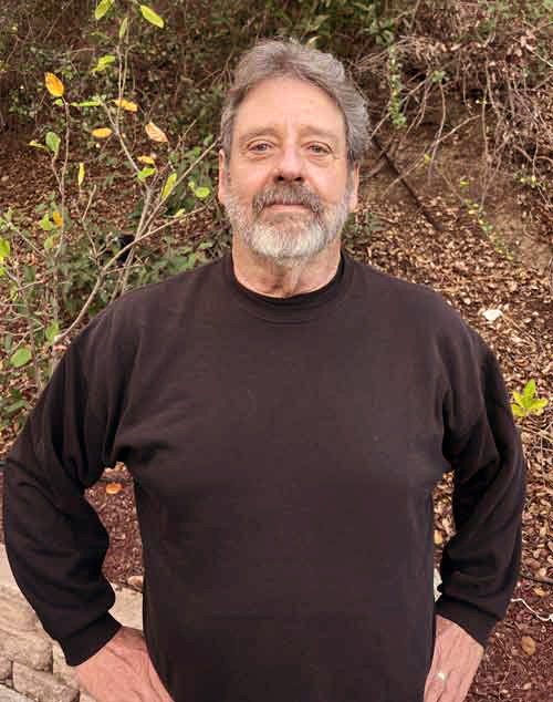 Man smiling with beard against a woodsy background
