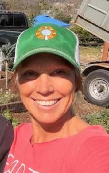Smiling woman in green ballcap with a garden and truck in the background