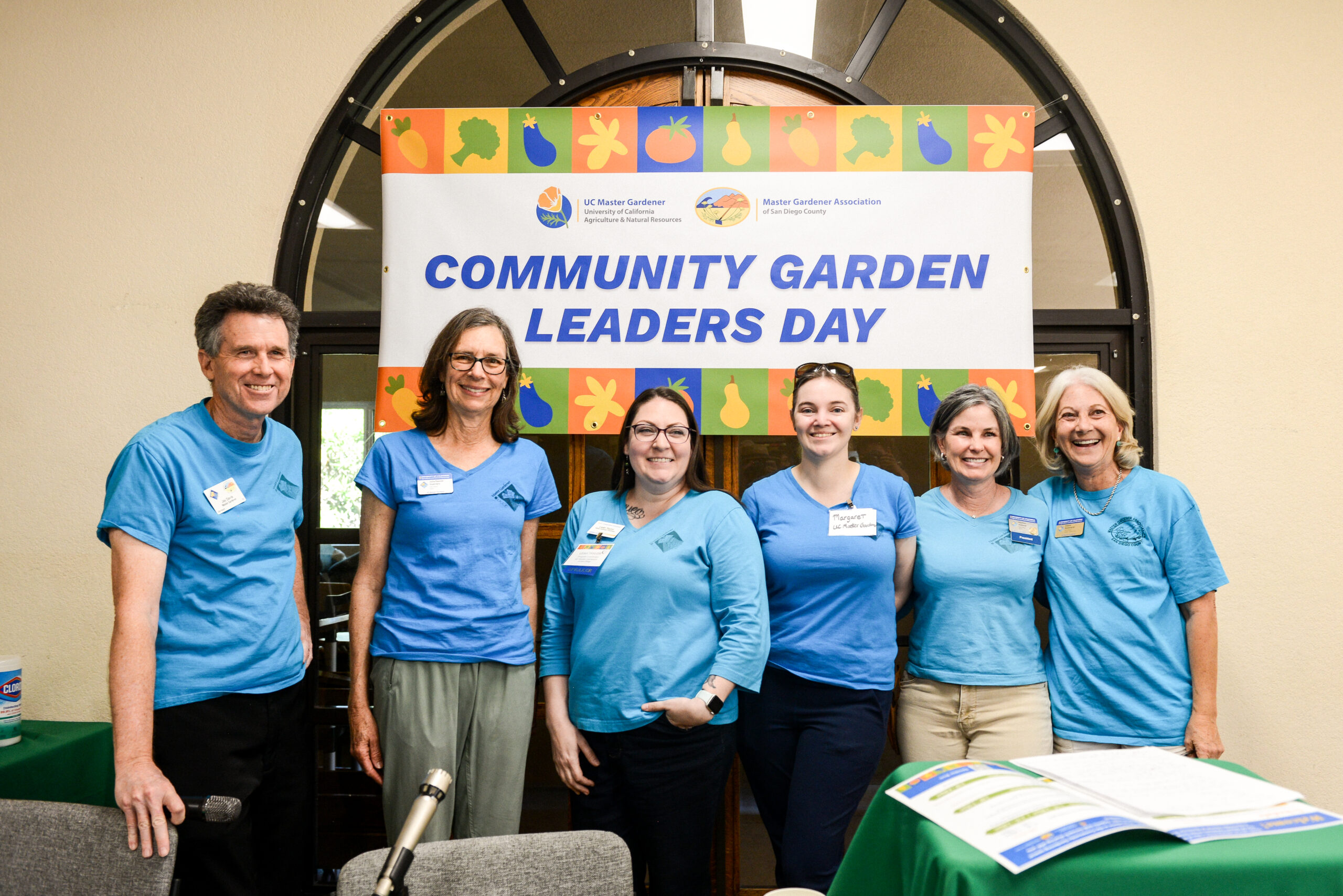 6 smiling master gardeners in matching blue t-shirts in front of Community Garden Leaders Day sign