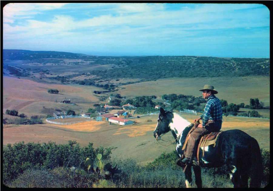 An historic photo, Leo Carrillo surveys the property he bought in 1937 for a working ranch and private retreat. In the valley below, whitewashed adobe buildings stand out against the undeveloped Carlsbad hills.